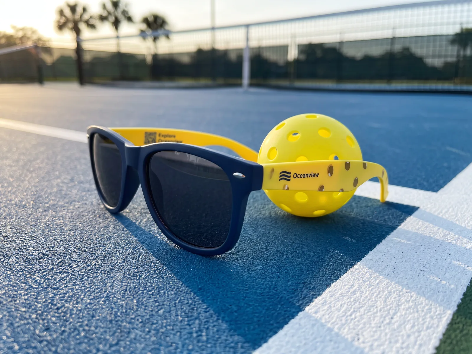 Oceanview's navy and ball-yellow pair resting on a blue pickleball court beside a yellow pickleball, near the kitchen line.